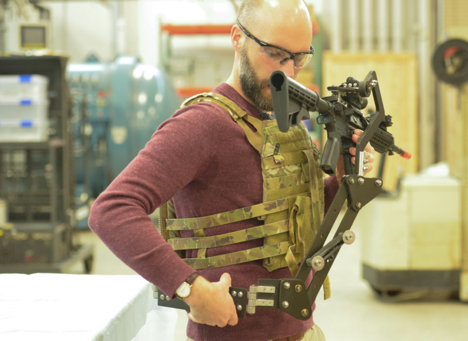 Army Research Lab engineer Dan Baechle demonstrates how to strap on the "Third Arm," a mechanical device designed to improve Soldiers' accuracy and reduce fatigue. (Photo Credit: U.S. Army photo by Joe Lacdan)
