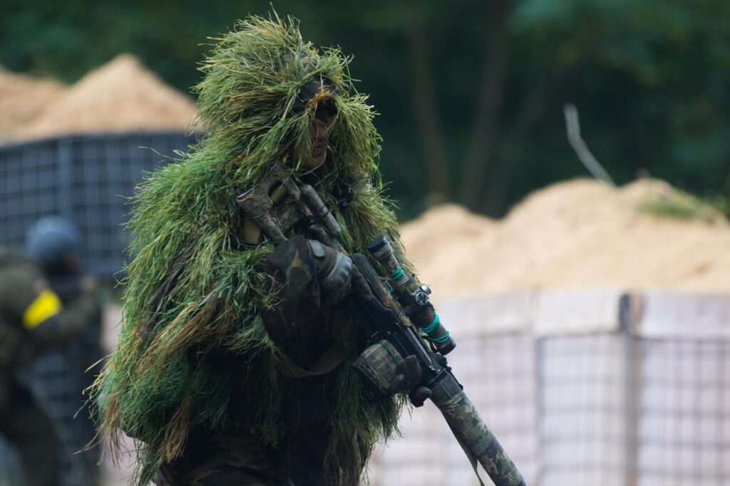 Sniper ucraino in tuta mimetica ghillie con fucile dotato di ottica durante l’esercitazione Pivnichnyi Burevii, vicino al confine bielorusso